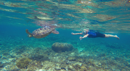 Green turtle with swimming woman in modern snorkeling equipment.