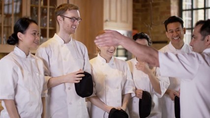  Professional chef talking to happy young trainees in cookery school