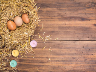 Brown eggs in hay nest. Rural eco background with brown chicken eggs, colored candles and straw on the background of old wooden planks Top view. Creative background for Easter cards or restaurant menu