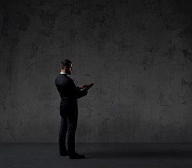 Businessman standing with computer tablet over dark wall background. Business, career job concept.