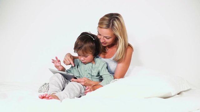 4 j&auml;hriger bub im bett mit kopfh&ouml;rern spielt mit dem tablet gemeinsam mit seiner mutter