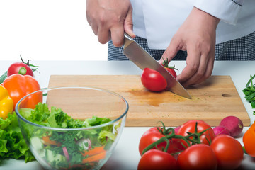 cook cuts a tomato for salad on a background of vegetables