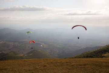Some colorful paragliders flying over a mountain scenery, with some faint sunrays.