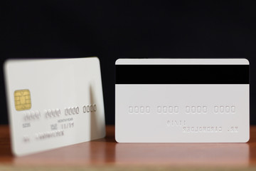 Two sides of white credit card with embossing on wooden table over black background