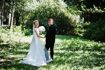 Stylish and gorgeous wedding couple walking outdoor at park on sunny weather.