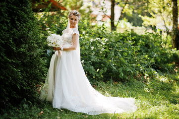 Awesome gorgeous blonde bride with wedding bouquet at hands at sunny day.