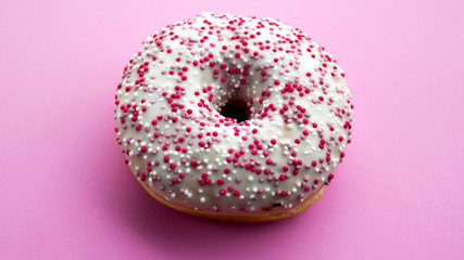 donut with colorful sprinkles on pink background.