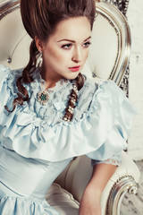 Indoors shot in the Marie Antoinette style. A young sexy girl in a lush blue retro dress with a...