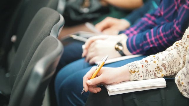 Students participating in a lecture and taking notes - people writing into their notebooks