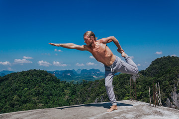 Yoga man standing in asana. Young fit male standing in asana and stretching body on ground with tropical views on background.