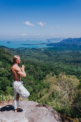 Man balancing on rock. Side view of male in white pants balancing on one leg with amazing tropical views on background.