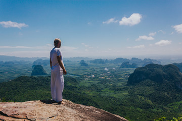 Male in white standing against tropical views. Back view of man in white clothing standing on high cliff and enjoying outstanding tropical views.