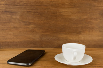 Cup,cup of coffee and smart phone on wooden board in front of brown wooden blur background