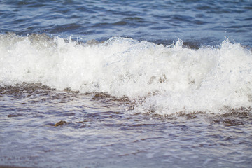 Cold blue sea water surf over seashore. Chilly sea wave splashes over coast.