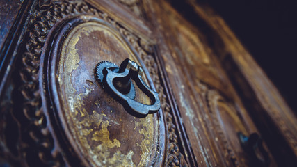 Antique metal handles knock on a vintage wooden carved door wicket.