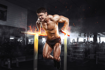 Fototapeta na wymiar Muscular bodybuilder working out in gym doing exercises on burning fire parallel bars. Concept sport