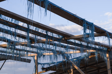 Fototapeta premium Wooden frame with thin pieces of torn blue fabric on an abandoned market on the background of sky with clouds, Ukraine.