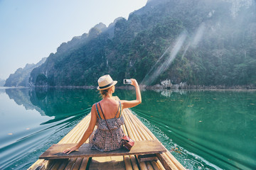 Travel and technology. Pretty young woman taking photo on smartphone sailing National Park lake on...