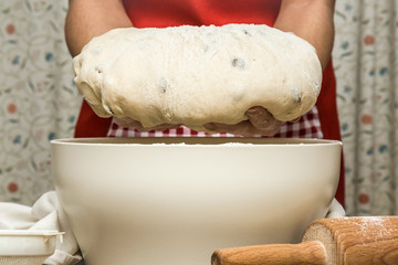 Hands holding a dough with raisins. It is ready for baking. Homemade pastries in the kitchen. Healthy eating lifestyle.