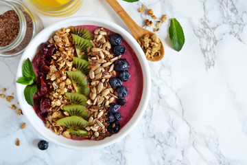 Berry smoothie with blueberries, kiwi fruit, sunflower seeds, granola with homemade yogurt on a marble background