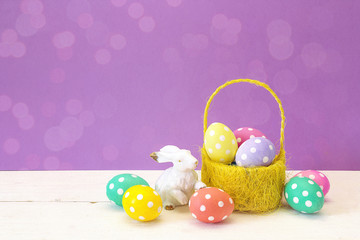 Yellow basket with Easter eggs and a rabbit on a purple background. Place for the text.