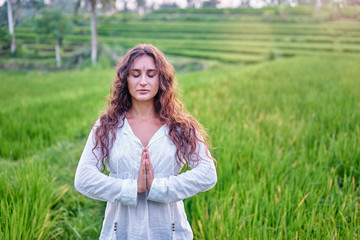 Yoga with view of green fields. Young woman with clasped hands. Concept of calm and meditation.