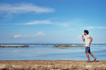 Sports lifestyle. Happy young african man jogging on the sea shore.