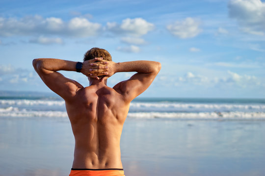 Holiday on the beach. Back view of relaxed young muscular man enjoying sea view.