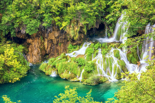 Plitvice Lakes National park, picturesque waterfall flows into the emerald lake surrounded by green summer forest, popular tourist destination in Croatia. Nature background for wallpaper or guide book