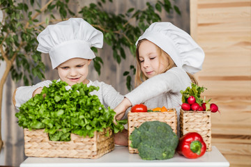 Handsome boy and beautiful young girl playing in the kitchen chefs. Healthy food. Vegetables