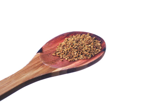 Fenugreek seeds on a brass spoon isolated on a white background.