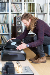 long haired man putting an lp record on the turntable