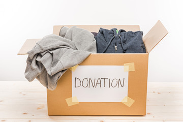 cardboard box with donation clothes on wooden table on white, donation concept