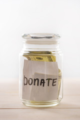 Close-up view of dollar banknotes in glass jar with donate lettering, donation concept