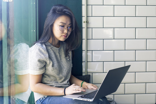 Attractive hipster girl wearing glasses is chatting with friends by using a laptop connected to the public wi-fi. Beauty blogger is observing the latest fashion trends by surfing the internet.