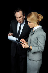 Serious businessman and businesswoman looking at clipboard with papers on black