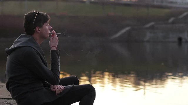 The young guy smoking near the river