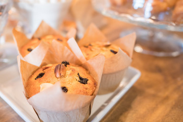 golden brown cupcake topped with raisin and cashew nut, wrapped with paper cup, on wooden brown table