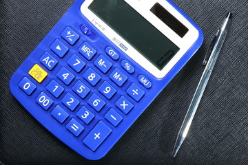 Close up photo of blue color solar and battery power calculator put beside the ball pen  on black leather surface background.
