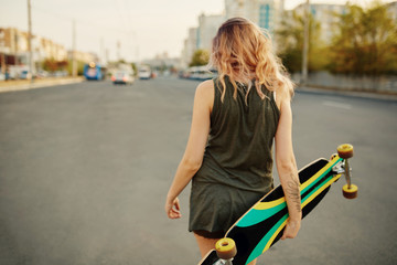 Beautiful young tattooed girl with longboard in sunny weather