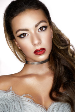 A young Asian girl with creative makeup, arrows and bright red lips with sparkles. A beautiful model with perfect skin in a fur coat made of artificial fur and a checker on neck. Beauty of the face.