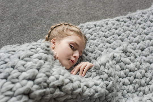 adorable girl lying on floor with grey knitted blanket and looking at camera
