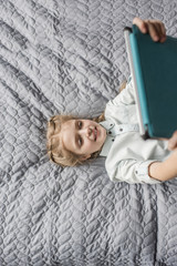 adorable girl using digital tablet and lying on bed at home