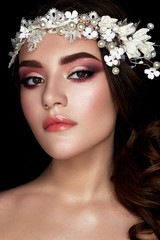 A young girl in the image of a bride with a floral wreath on her head and curls. A beautiful model with a bright makeup and perfect skin. Beauty of the face. Photo is taken in a studio.