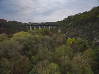 Aerial shot of the canyon of the Smotrych River towards the Novoplanivskyi Bridge in Kamianets-Podilski Ukraine. The shot is taken in autumn with the canyon trees looking colourful