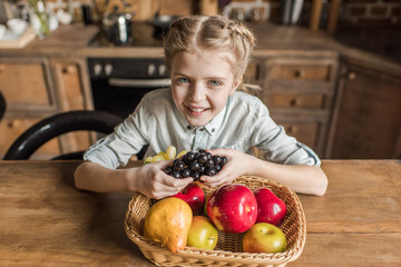 Fototapeta premium adorable girl with different fruits sitting at table in kitchen