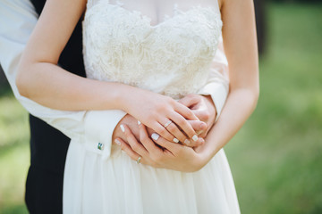 The groom in a shirt hugs a bride in a white dress and holds her hands, the bride on her finger has an wedding ring