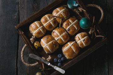 Hot cross buns in wooden tray served with butter, knife, blueberries, easter eggs, birch branch...