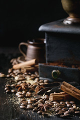 Black roasted coffee beans and grind with spices cinnamon, anise, cardamom, clove and brown sugar. With black vintage coffee grinder, scoops and terracota cup over wood burnt background.