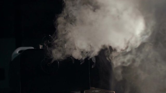 Smoke machine in action, slow motion. White smoke trail isolated on black background.
